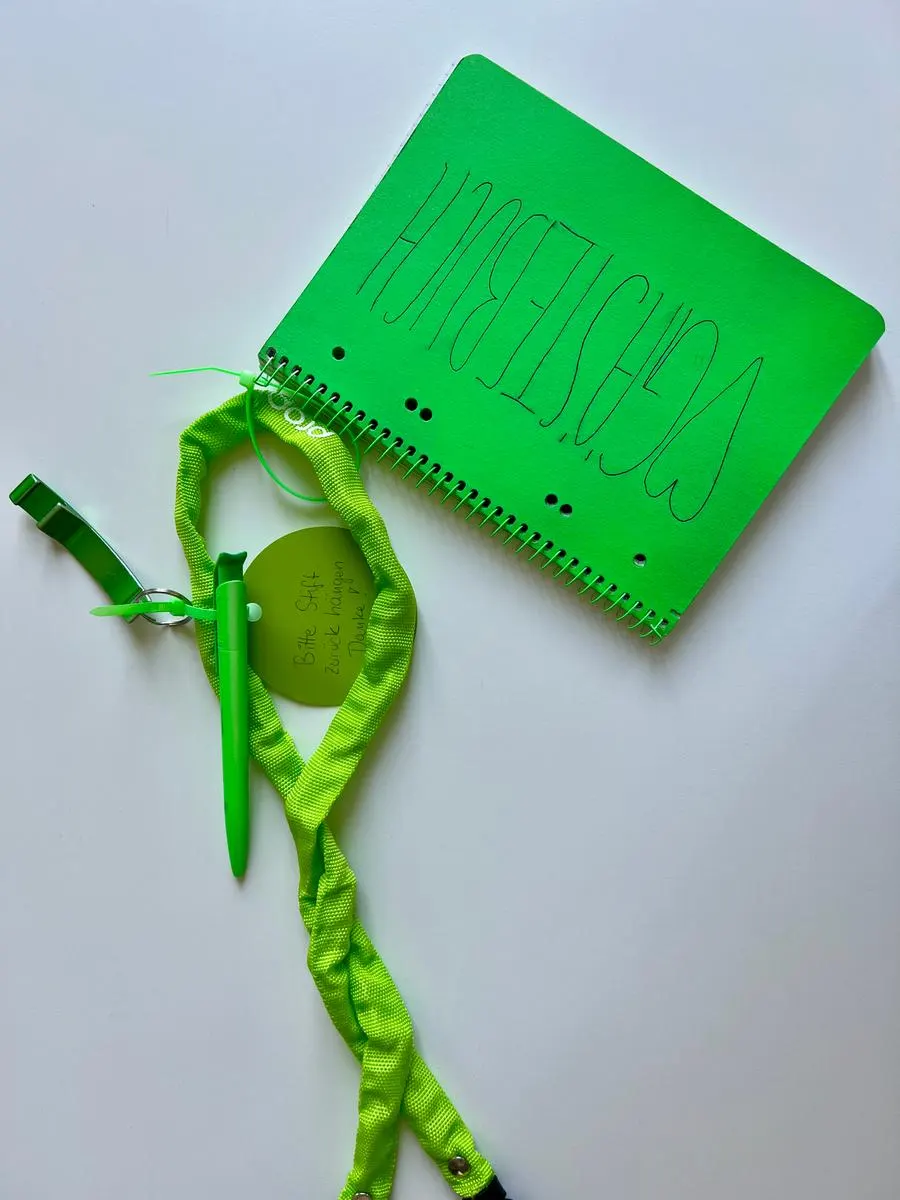 Das neongrüne Gästebuch mit der Aufschrift „Gästebuch“, daran eine grün besprühte Fahrradkette und ein Stift.