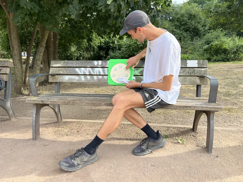 Ein Mann auf einer Parkbank liest einen Zettel aus der grünen Redekiste an der Rückenlehne.