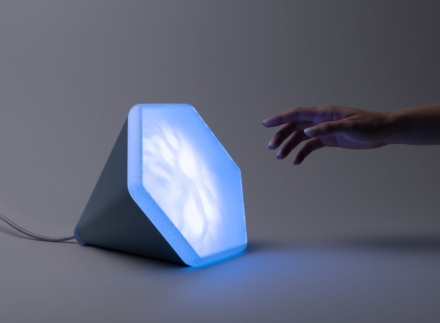 Nemus in blauer Lichtkomposition, eine Hand nähert sich der leuchtenden Fläche mit dem fraktalen Schattenmuster.